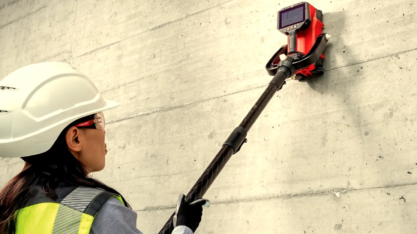 Surveyor using Hilti PS300 ground-penetrating radar to scan a concrete wall on a construction site